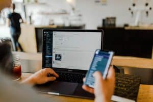 Persoon werkt op een laptop terwijl iemand anders een smartphone vasthoudt in een café